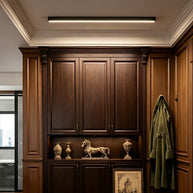 Slim linear LED ceiling light with a black body, fitted along a ceiling above dark wooden cabinets.