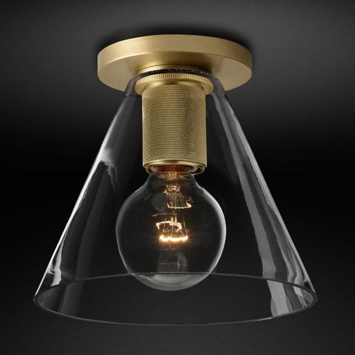 Flush-mount ceiling light with a brass ceiling plate, knurled holder and a clear cone-shaped glass shade.