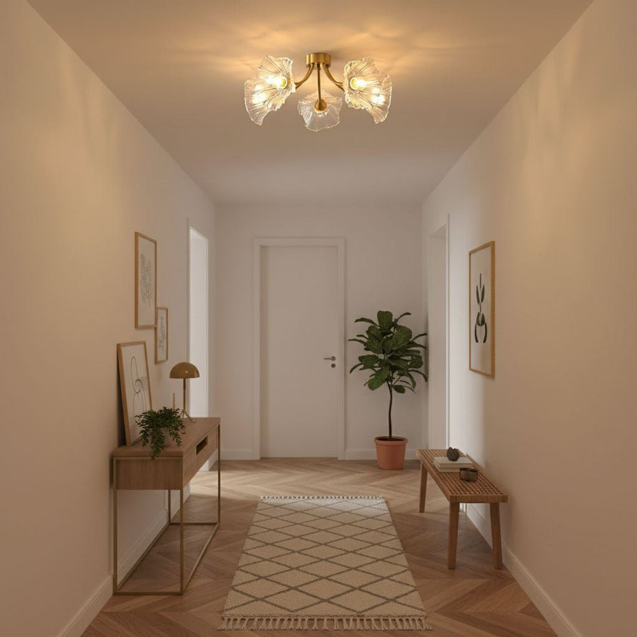 Flush-mount ceiling lamp with curved brass arms holding clear ribbed flower-shaped glass shades lit on a hallway ceiling.