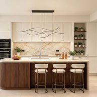 Linear pendant light made of wavy black LED bars hung from a slim rectangular canopy above a kitchen island with cream cabinets.