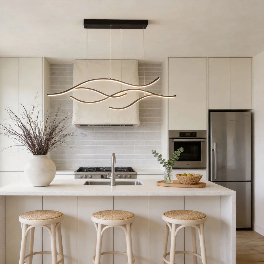 Linear pendant light made of wavy black LED bars hung from a slim rectangular canopy above a kitchen island with rattan stools.