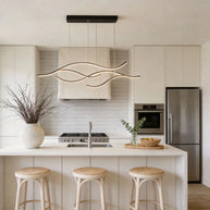Linear pendant light made of wavy black LED bars hung from a slim rectangular canopy above a kitchen island with rattan stools.