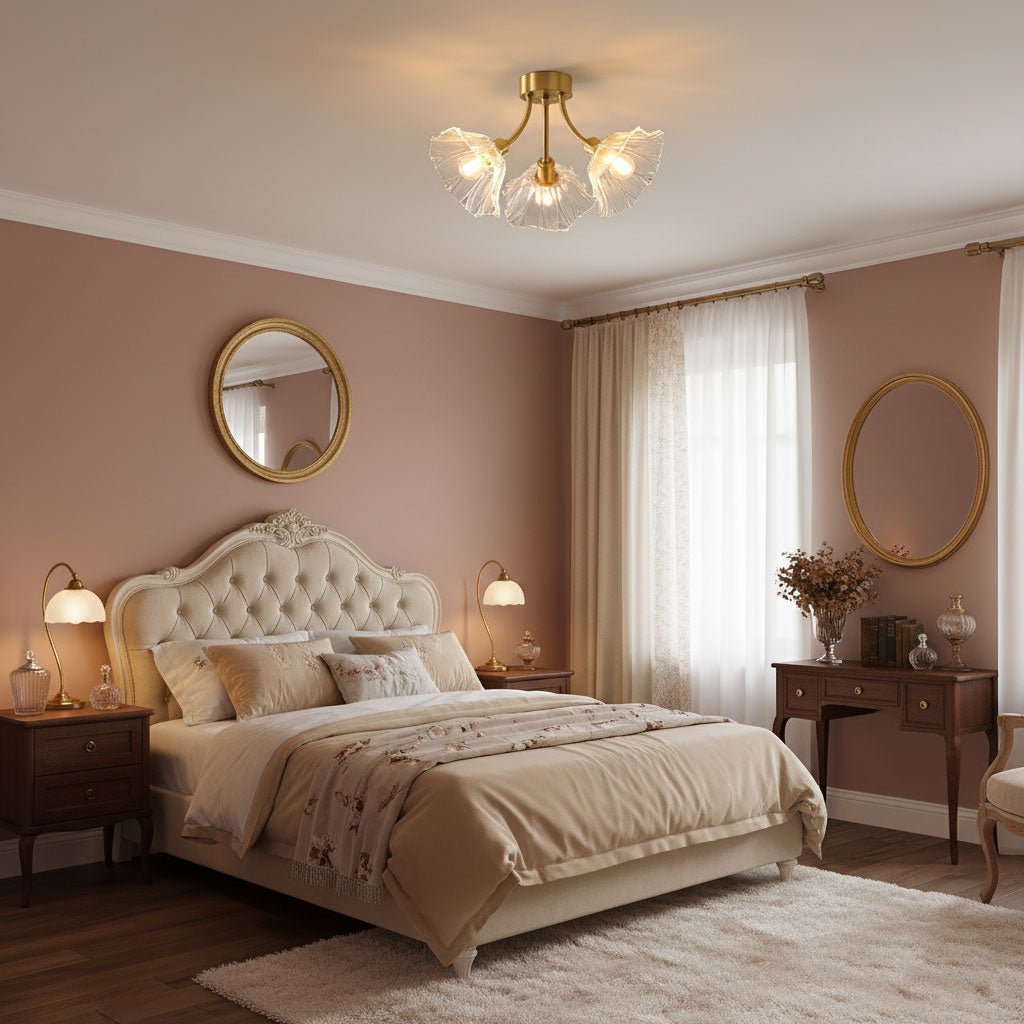 Flush-mount ceiling lamp with curved brass arms holding clear ribbed flower-shaped glass shades lit above a bed in a pink bedroom.