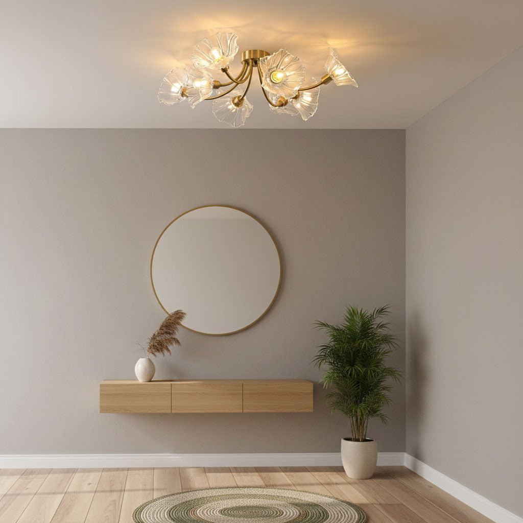 Flush-mount ceiling lamp with curved brass arms holding clear ribbed flower-shaped glass shades lit above a sideboard and round mirror.