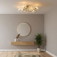 Flush-mount ceiling lamp with curved brass arms holding clear ribbed flower-shaped glass shades lit above a sideboard and round mirror.