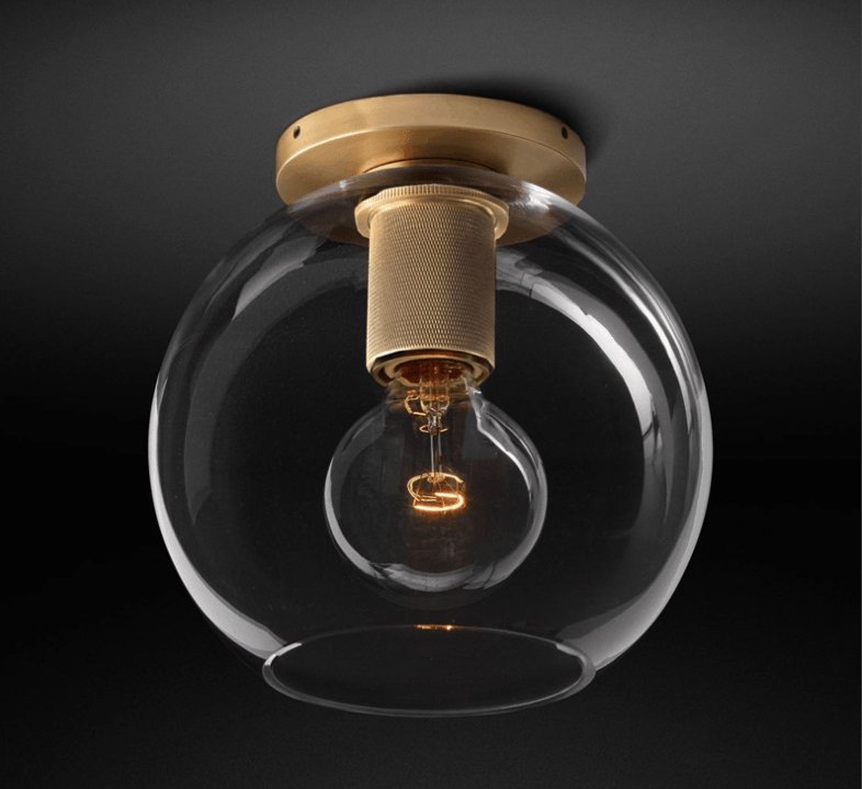 Flush-mount ceiling light with a brass ceiling plate and a clear round glass shade.