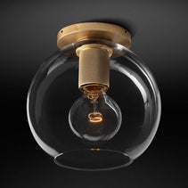 Flush-mount ceiling light with a brass ceiling plate and a clear round glass shade.