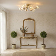 Flush-mount ceiling lamp with curved brass arms holding clear ribbed flower-shaped glass shades lit above a console table and mirror.