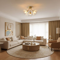 Flush-mount ceiling lamp with curved brass arms holding clear ribbed flower-shaped glass shades lit on a ceiling above a living room.