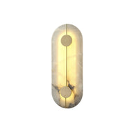 Wall light with a tall rounded alabaster panel, a slim brass rod and two brass discs lit on a white background, shown small.