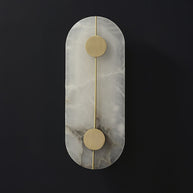Wall light with a tall rounded alabaster panel, a slim brass rod and two brass discs, unlit, on a dark background.