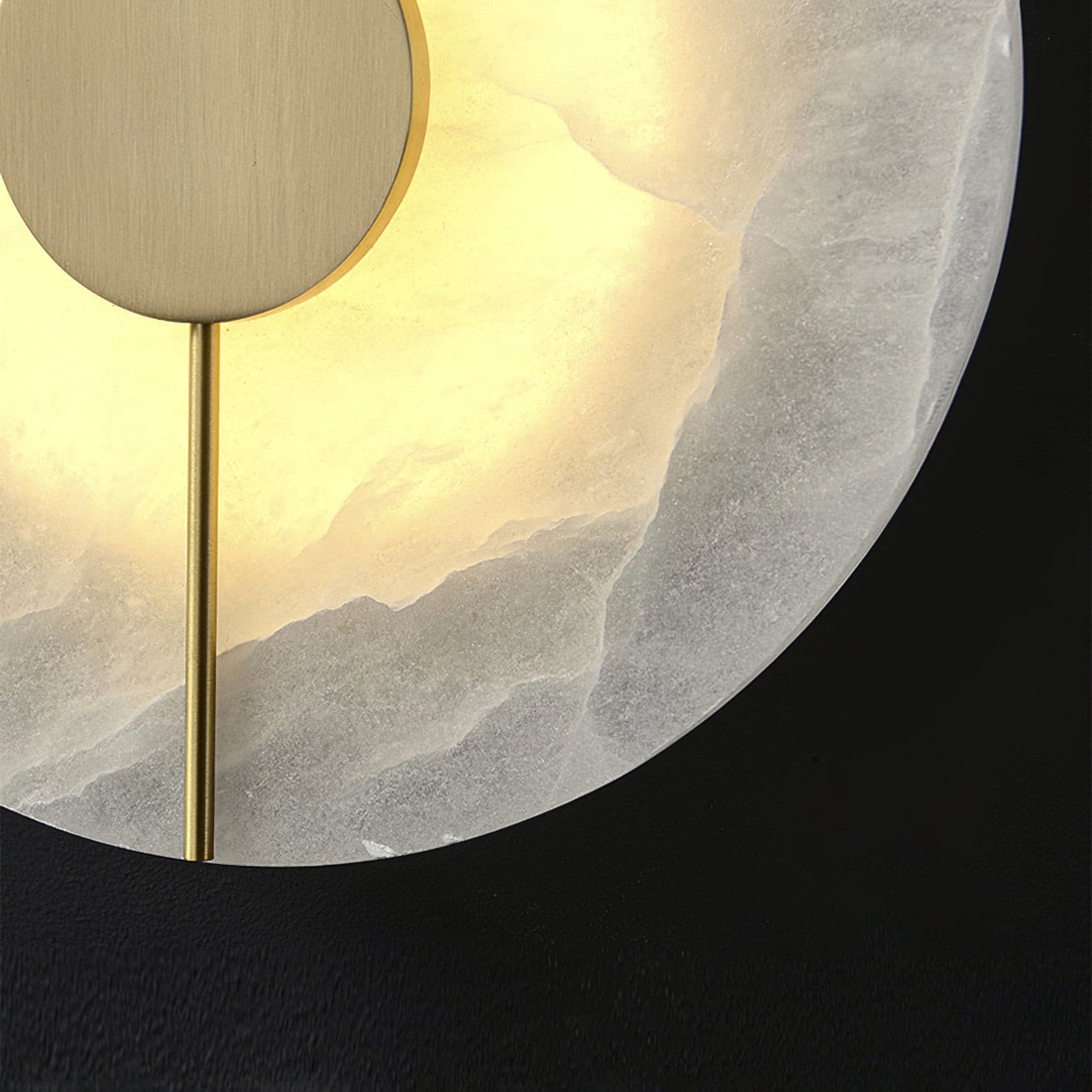 Close view of the lit alabaster disc and the brass rod running across it.