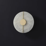 Wall light with a round veined alabaster disc, a slim brass rod and a brass centre disc, unlit, on a dark background.