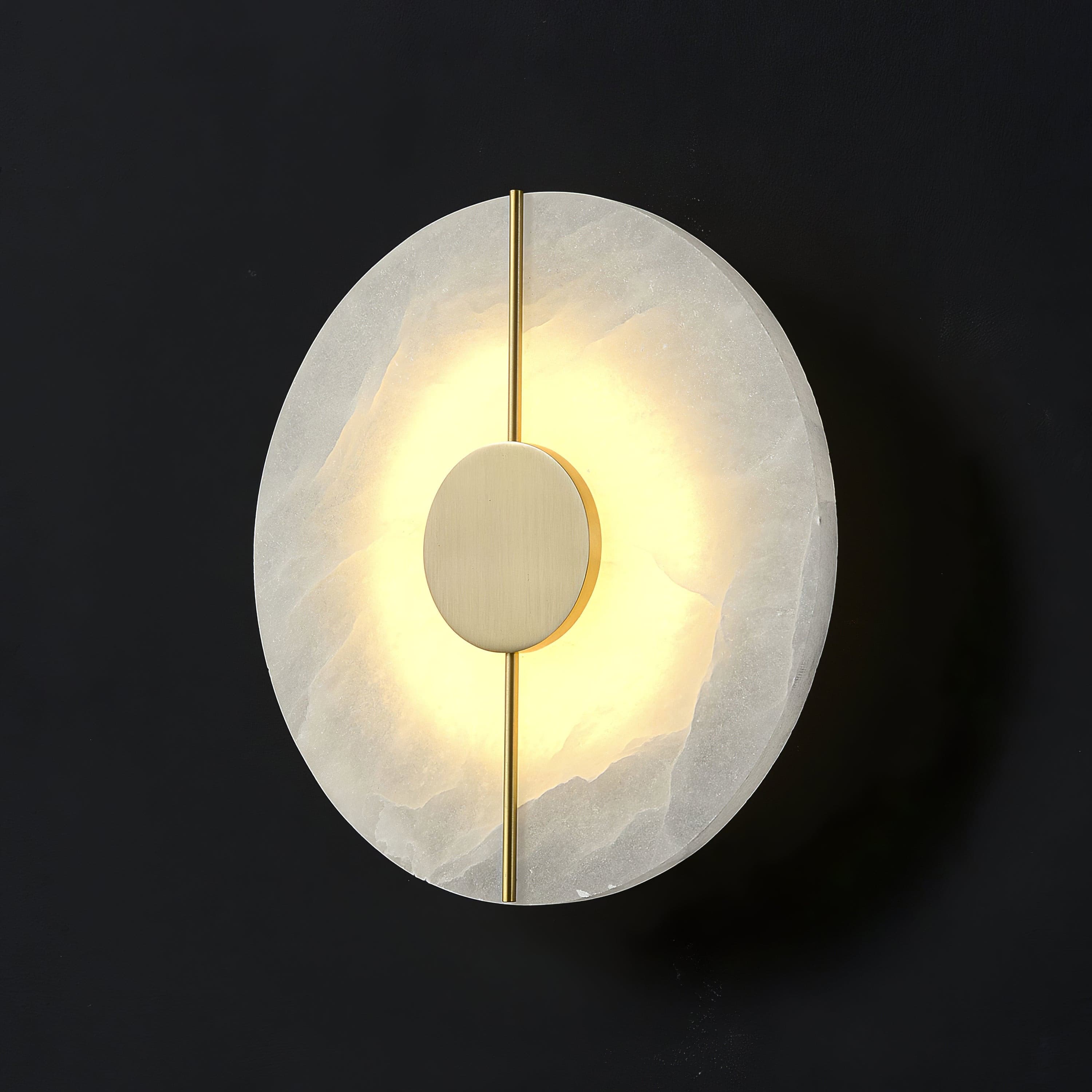 Wall light with a round veined alabaster disc, a slim brass rod and a brass centre disc lit on a dark background, seen close.