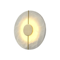 Wall light with a round veined alabaster disc, a slim brass rod and a brass centre disc lit on a white background.