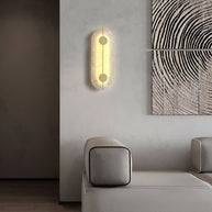 Wall light with a tall rounded alabaster panel, a slim brass rod and two brass discs lit beside a sofa and framed artwork.