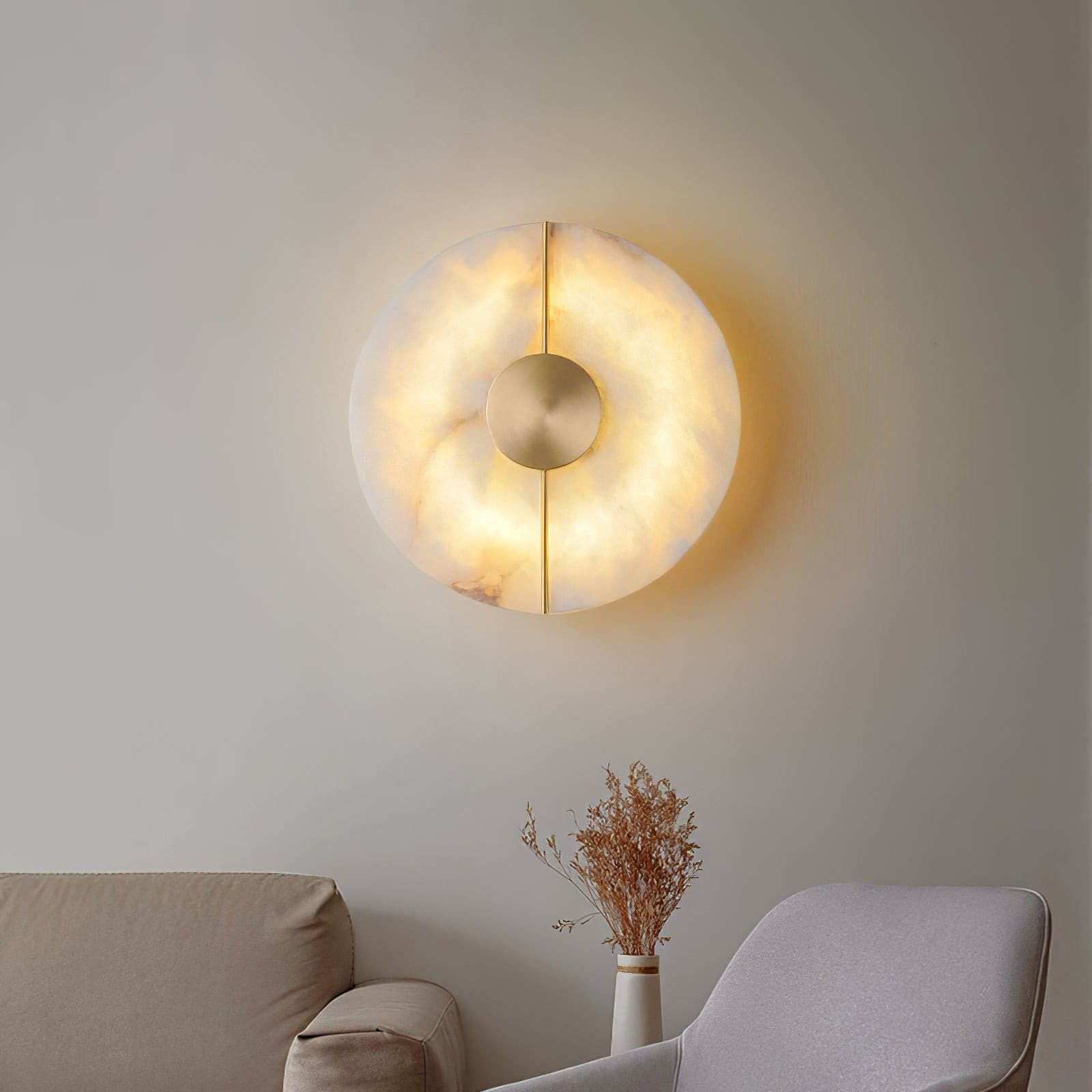 Wall light with a round veined alabaster disc, a slim brass rod and a brass centre disc lit above a sofa and an armchair.