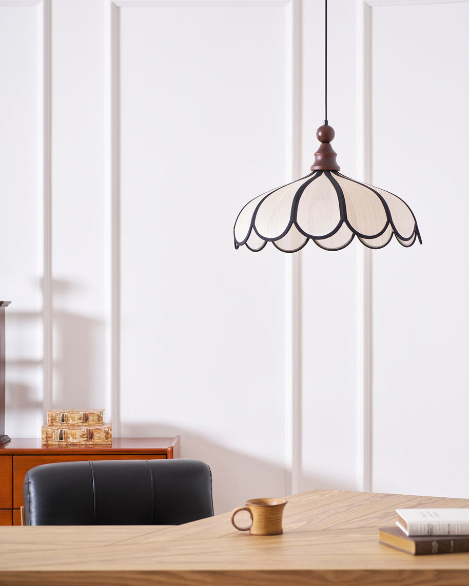 Pendant light with a scalloped beige shade, dark ribs and a turned walnut-coloured wooden top lit above a wooden table.