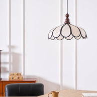 Pendant light with a scalloped beige shade, dark ribs and a turned walnut-coloured wooden top lit above a wooden table.