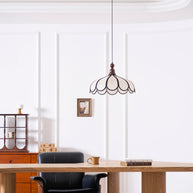 Pendant light with a scalloped beige shade, dark ribs and a turned walnut-coloured wooden top hanging in a panelled room above a wooden desk.