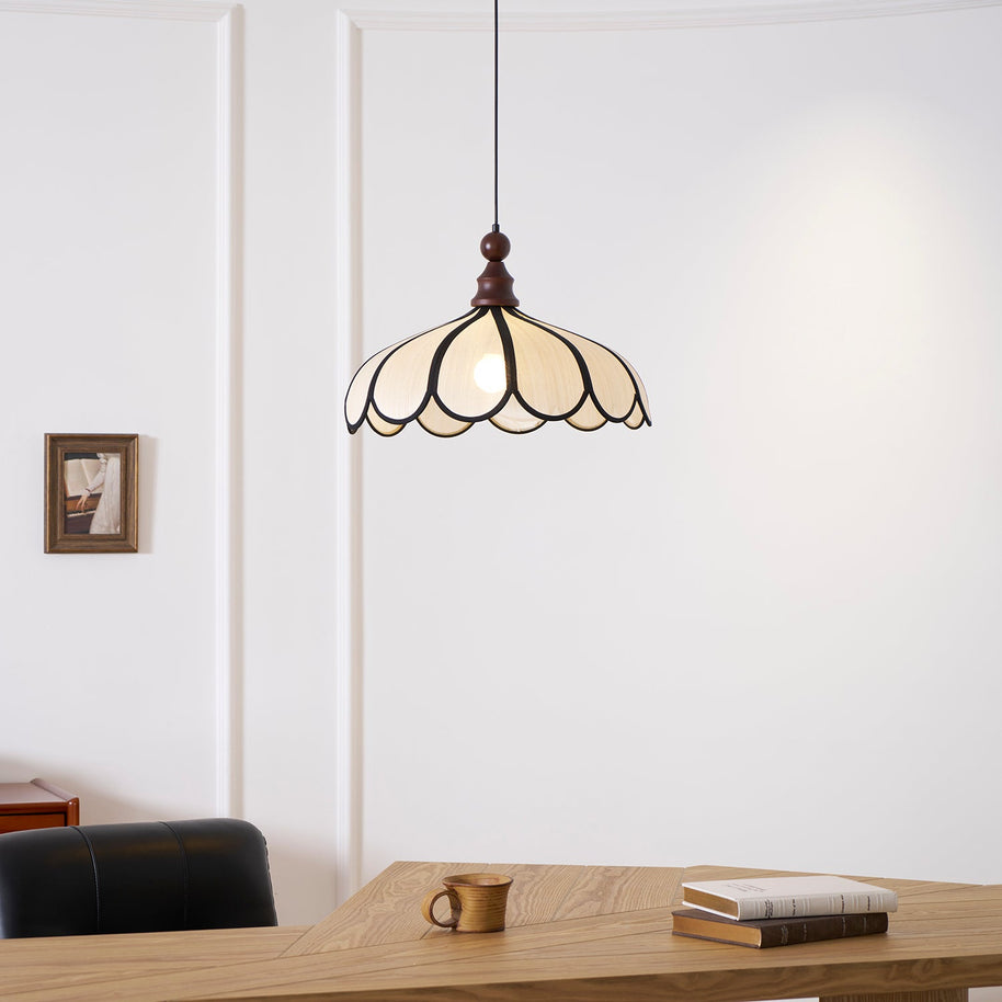 Pendant light with a scalloped beige shade, dark ribs and a turned walnut-coloured wooden top lit above a wooden table, seen close.