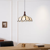 Pendant light with a scalloped beige shade, dark ribs and a turned walnut-coloured wooden top lit above a wooden table, seen close.