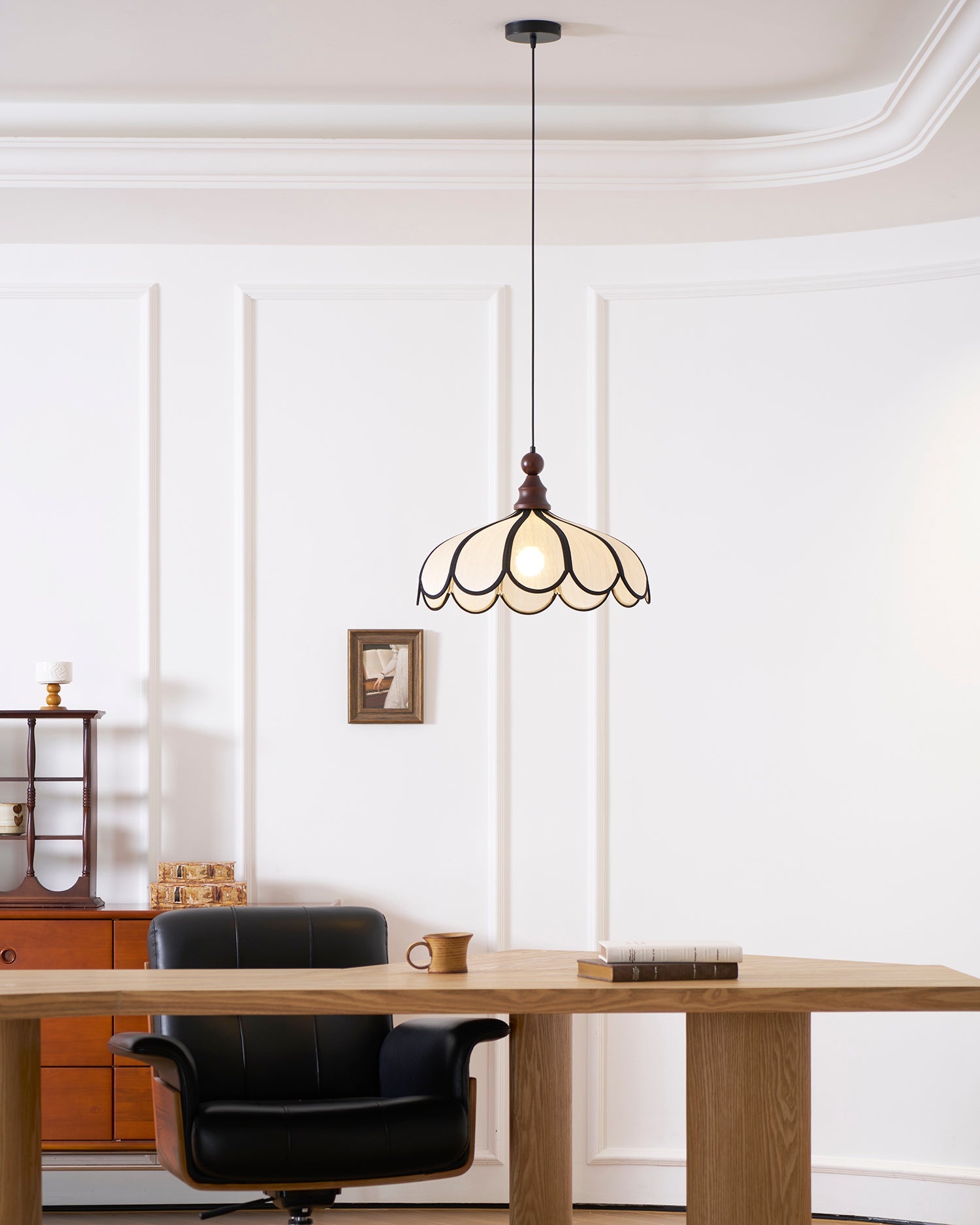 Pendant light with a scalloped beige shade, dark ribs and a turned walnut-coloured wooden top lit in a panelled room above a desk.