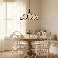 Pendant light with a scalloped beige shade, dark ribs and a turned walnut-coloured wooden top above a round dining table with white chairs.