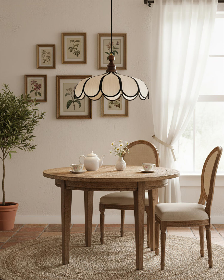 Pendant light with a scalloped beige shade, dark ribs and a turned walnut-coloured wooden top above a round table below framed botanical prints.