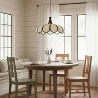 Pendant light with a scalloped beige shade, dark ribs and a turned walnut-coloured wooden top hanging above a round dining table in a panelled room.