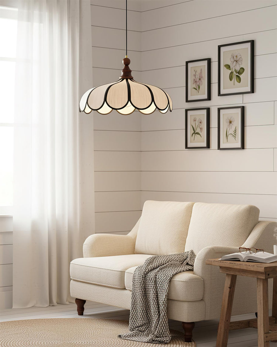 Pendant light with a scalloped beige shade, dark ribs and a turned walnut-coloured wooden top hanging above a cream sofa beside framed botanical prints.