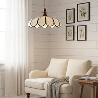 Pendant light with a scalloped beige shade, dark ribs and a turned walnut-coloured wooden top hanging above a cream sofa beside framed botanical prints.