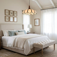 Pendant light with a scalloped beige shade, dark ribs and a turned walnut-coloured wooden top lit above a bed in a room with a sloped ceiling.