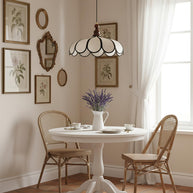 Pendant light with a scalloped beige shade, dark ribs and a turned walnut-coloured wooden top above a small round table with two cane chairs.