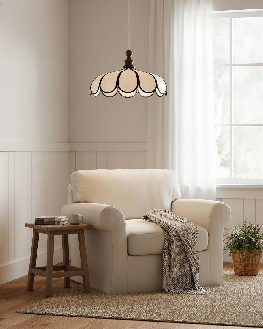 Pendant light with a scalloped beige shade, dark ribs and a turned walnut-coloured wooden top above a cream armchair by a window.