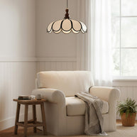 Pendant light with a scalloped beige shade, dark ribs and a turned walnut-coloured wooden top above a cream armchair by a window.