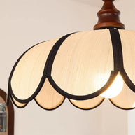 Close view of the lit pendant light with a scalloped beige shade, dark ribs and a turned walnut-coloured wooden top from below, showing the ribs and scalloped hem.