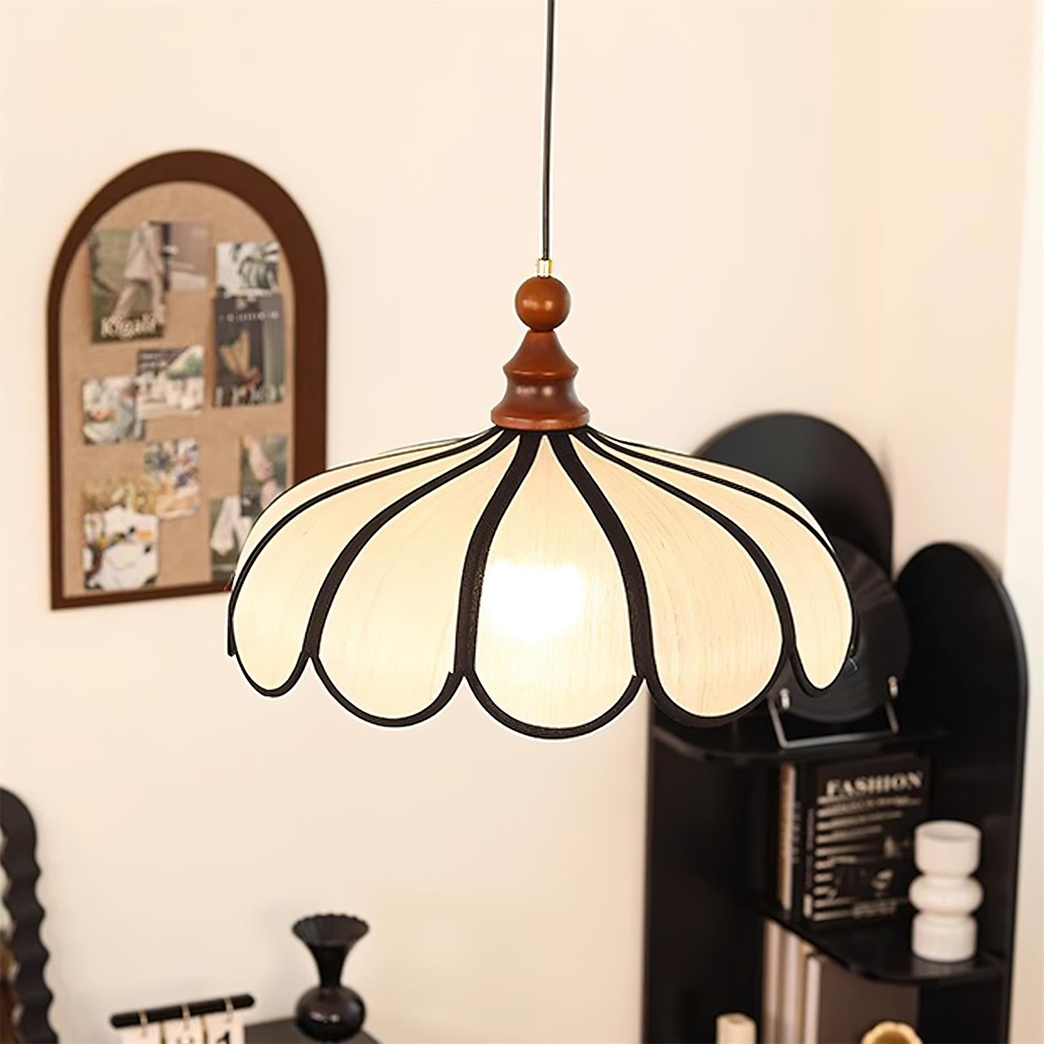 Pendant light with a scalloped beige shade, dark ribs and a turned walnut-coloured wooden top lit, seen close in front of a pinboard and shelving.