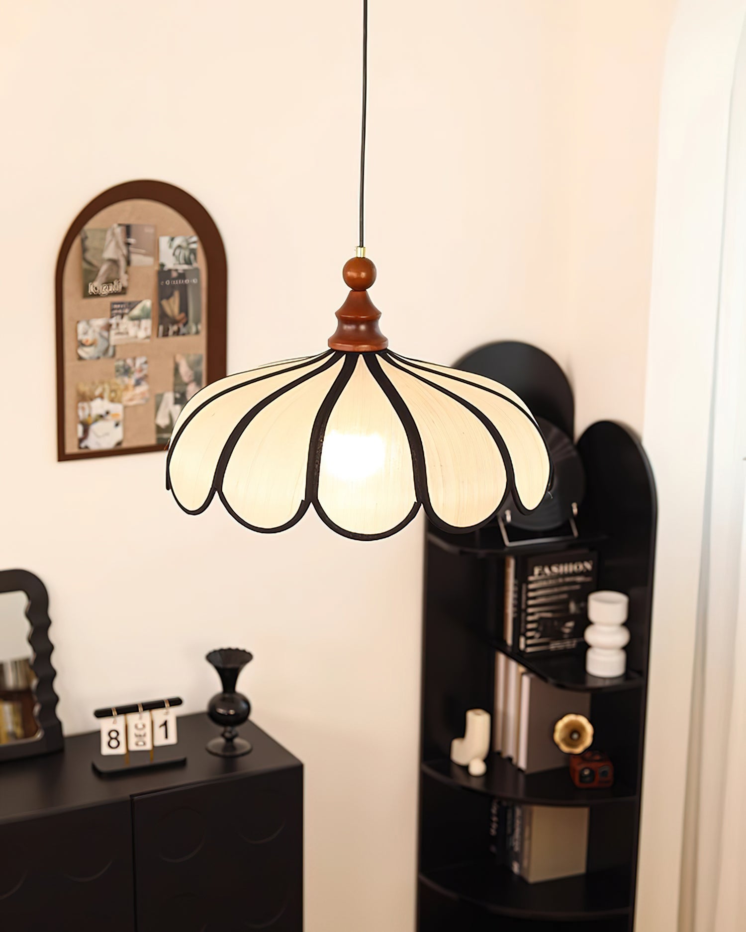 Pendant light with a scalloped beige shade, dark ribs and a turned walnut-coloured wooden top hanging beside a pinboard and a dark cabinet.