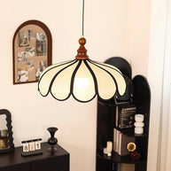 Pendant light with a scalloped beige shade, dark ribs and a turned walnut-coloured wooden top hanging beside a pinboard and a dark cabinet.