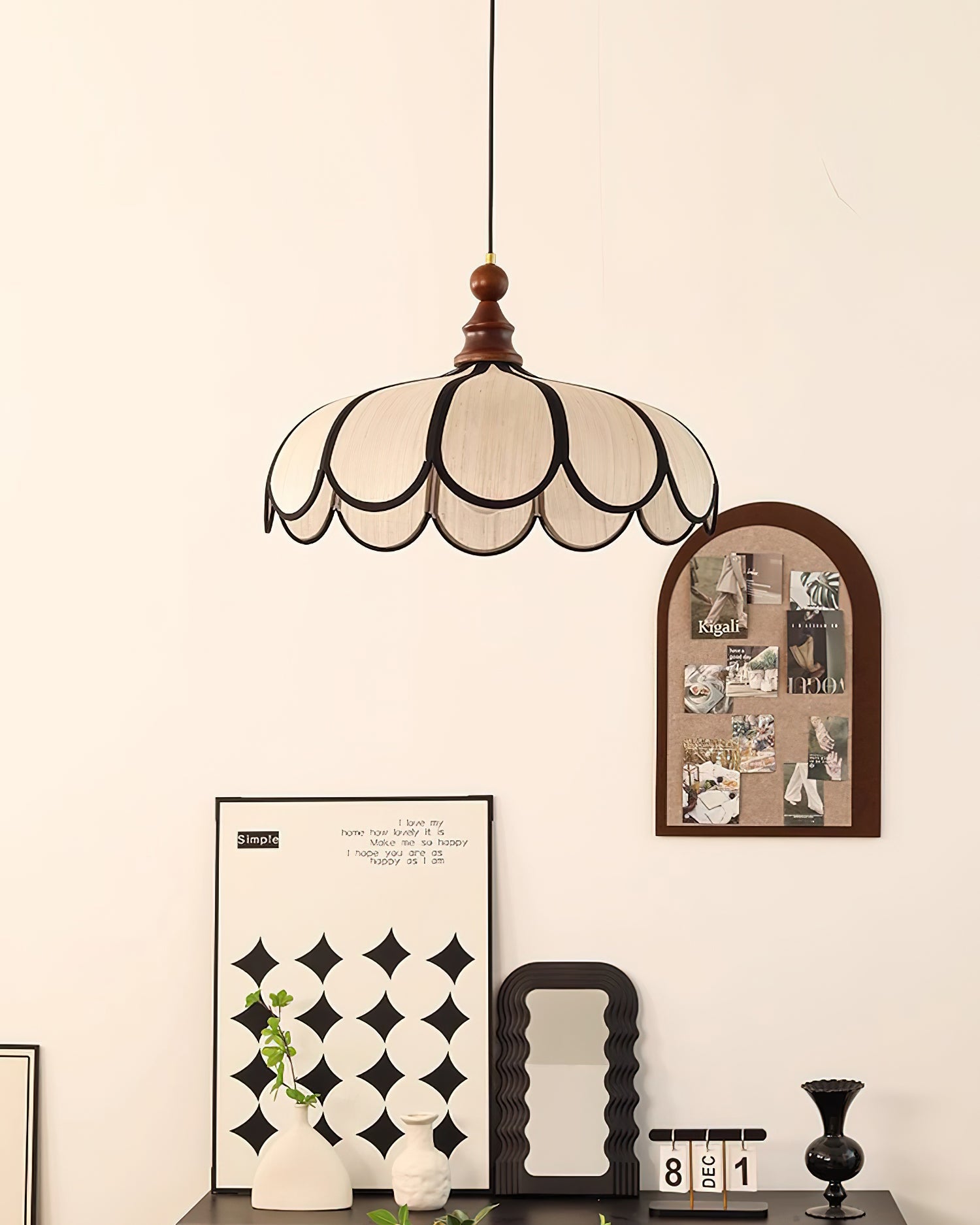 Pendant light with a scalloped beige shade, dark ribs and a turned walnut-coloured wooden top hanging beside a pinboard and a shelf of ornaments.