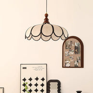 Pendant light with a scalloped beige shade, dark ribs and a turned walnut-coloured wooden top hanging beside a pinboard and a shelf of ornaments.
