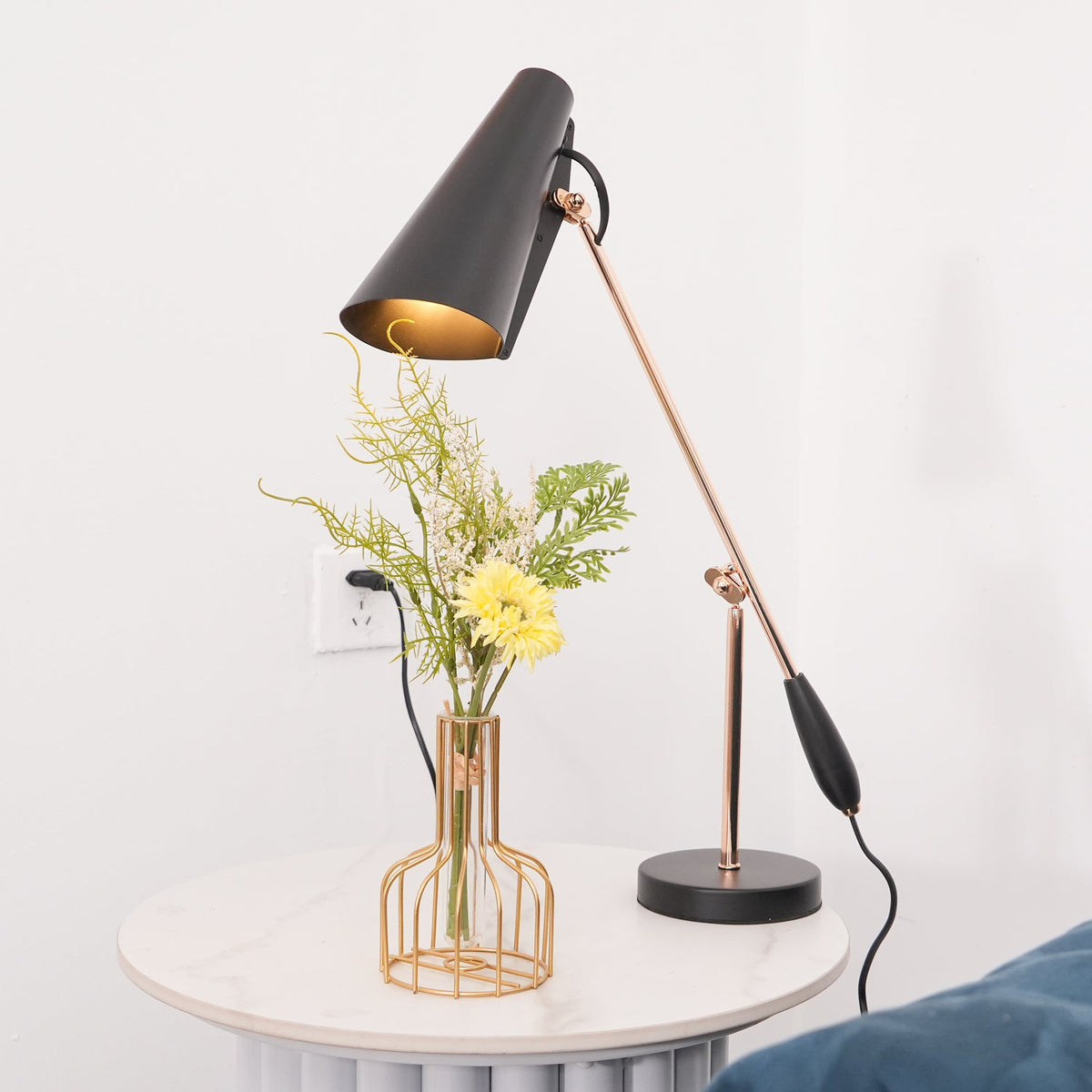 Avielle Table Lamp in gold and black, lit above a marble side table with flowers