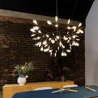 Comvilo firefly LED chandelier in black, lit above a dining table against an exposed brick wall