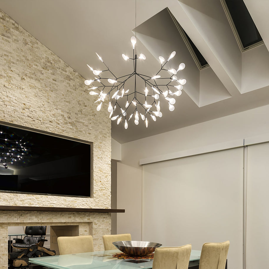 Comvilo firefly LED chandelier in black, lit above a glass dining table in a room with a stone fireplace