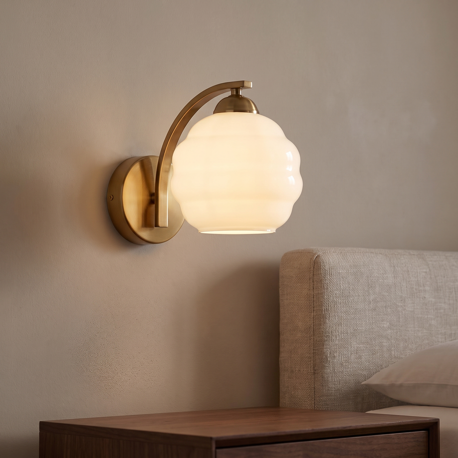 Brass wall light with a scalloped opal glass shade in a neutral bedroom.