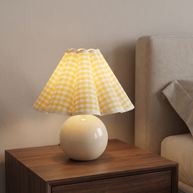 Table lamp with a round white base and yellow plaid pleated shade.