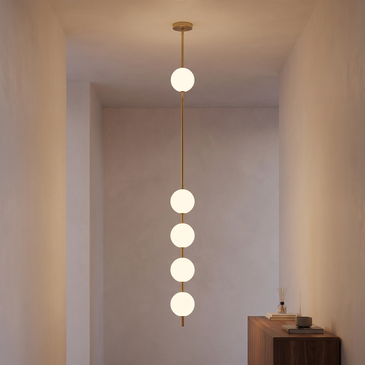 Ivrelle Vertical Globe Pendant in brass with five white opal globes, lit, hanging in a plaster entry hall beside a walnut console.