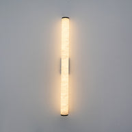 Wall lamp with a long pale veined alabaster tube and a black bracket lit, shown large on a plain wall.