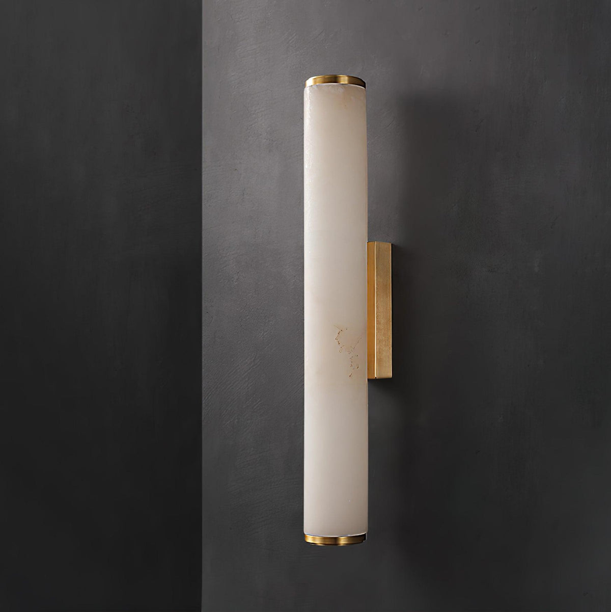 Wall lamp with a long pale veined stone-look tube and a gold-toned bracket, unlit, on a dark grey wall.